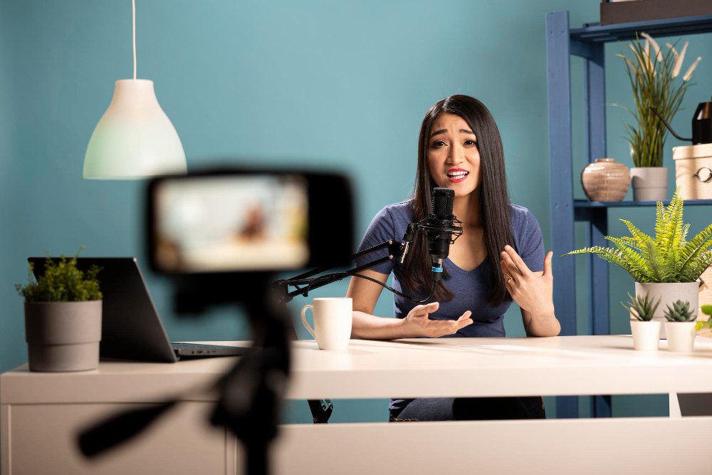 Mulher apresentando conteúdo em estúdio com microfone e câmera, criando estratégias de marketing promocional digital.