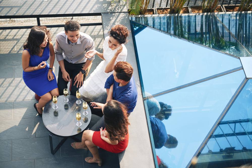 Grupo de profissionais conversando ao redor de uma mesa com bebidas durante um evento corporativo ao ar livre.
