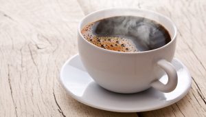 Xícara branca com café quente soltando vapor sobre mesa de madeira, referência visual para frases para xícaras de café simples e acolhedoras.